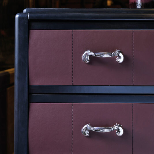 A close-up of the Luxury Leather Horse Handle Chest Of Drawers showcasing its opulent design. The chest features two dark brown leather-paneled drawers adorned with shiny, ornate silver horse handles. The cabinet has a black frame, emphasizing the intricate craftsmanship of the handles.
