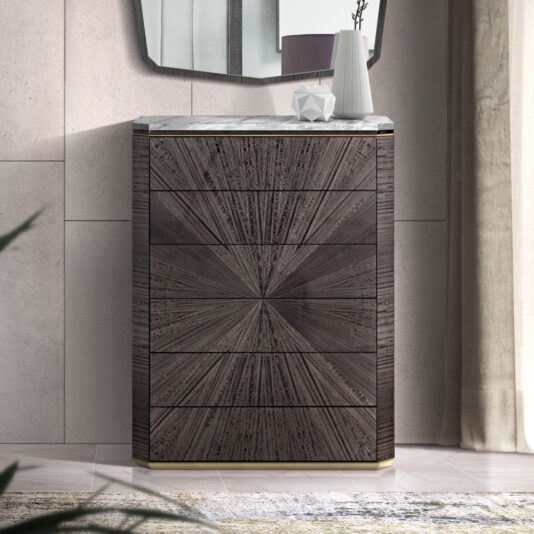 A modern, Luxury Marble Tallboy Chest Of Drawers with a dark wood finish and sunburst pattern on the front sits against a beige tiled wall. On top of the tallboy is a small, angular decorative object and a tall white vase with a single branch. A portion of a round mirror is visible above.