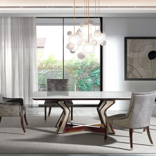 A modern dining room featuring the Luxury Marble Top Dining Table with a geometric wooden base and four upholstered chairs. A cluster of spherical pendant lights hangs above the table. Large windows with sheer curtains offer an outdoor view, while a contemporary abstract painting adorns the wall.