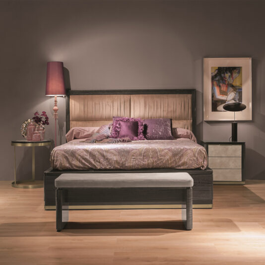 A luxury modern bedroom features a Luxury Modern Upholstered Bed with a tufted headboard and purple bedding, accented with throw pillows. On either side, there are nightstands with a lamp and decor. A bench sits at the foot of the bed, and a colorful abstract painting hangs on the wall.