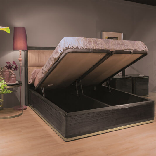 The Luxury Modern Upholstered Bed, featuring a dark frame and tufted headboard, adds elegance to a luxury bedroom. The bed's lifted mattress reveals convenient storage space underneath. Beside it, a nightstand holds a purple vase with flowers and is complemented by a tall purple floor lamp, enhancing the modern aesthetic.