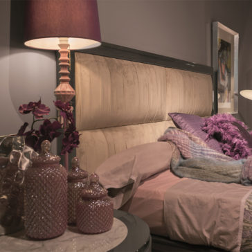 Luxury Modern Upholstered Bed A cozy bedroom features the Luxury Modern Upholstered Bed with beige fabric, adorned with pink and purple bedding. A matching lamp with a pink shade and ceramic jars sit on the bedside table. Purple flowers add a touch of decoration. The room is softly lit, exuding a tranquil ambiance.