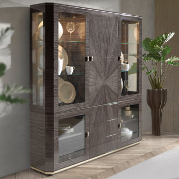 The Luxury Modern Display Cabinet features a glossy dark wood finish, complete with glass shelves and glass doors that elegantly showcase various tableware such as plates, bowls, and glasses. This stunning piece stands on a beige herringbone-patterned wooden floor next to a tall potted plant.