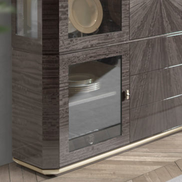 A close-up of the Luxury Modern Display Cabinet reveals its glossy, dark wood finish. The cabinet features glass doors showcasing plates within and sleek, horizontal lines. It stands on a light-colored base with a herringbone parquet floor in the background.