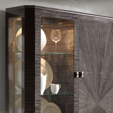 The Luxury Modern Display Cabinet, crafted in dark wood with a glossy finish and glass doors, elegantly showcases neatly arranged white and cream-colored dishware inside. Its shelves are adorned with plates, bowls, wine glasses, and cups for a sophisticated display.