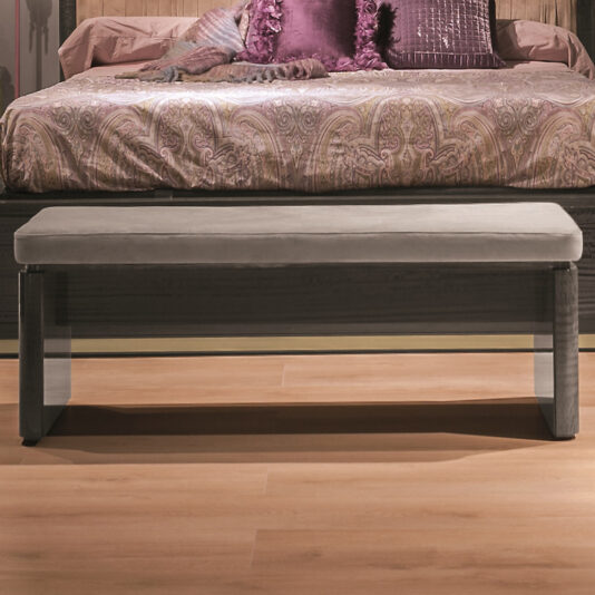A luxury modern bedroom showcases the Luxury Modern Upholstered Bed adorned with an ornate paisley-patterned bedspread and plush purple cushions at the headboard. In the foreground, a sleek, upholstered bench with metallic legs is positioned at the foot of the bed, all set on a wooden floor.