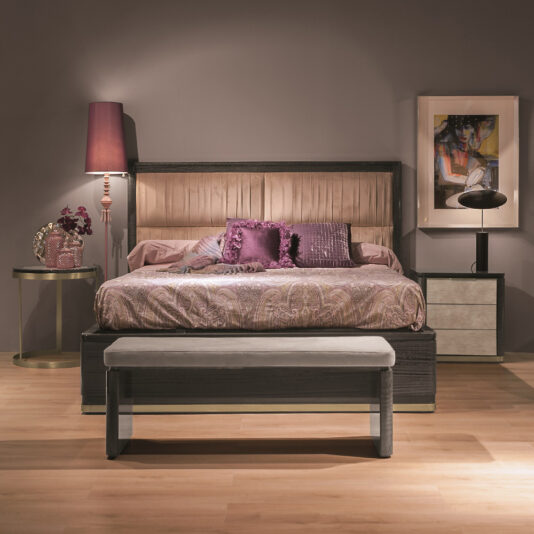 A luxury modern bedroom features the elegant Luxury Modern Upholstered Bed, adorned with a plush, padded headboard and dressed in rich purple and pink bedding. The bed is complemented by both round and rectangular nightstands, each holding a stylish lamp and an eye-catching art piece. At the foot of the bed rests a chic bench, while a decorative purple vase adds a vibrant touch to the room.
