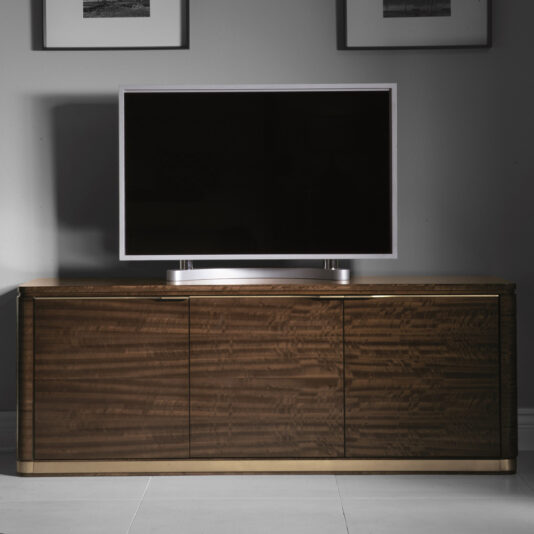 A modern flat-screen TV is elegantly perched on the Luxury TV Unit With Brass Trim. The sleek design of this large, dark wooden console boasts a smooth surface and ample storage cabinets. In the background, a gray wall is adorned with two framed pictures, all gently illuminated by soft lighting.