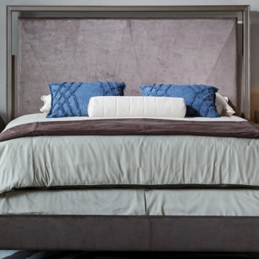 Luxury Metal Frame King Size Bed The Luxury Metal Frame King Size Bed features a neatly made setup with a large upholstered headboard. The bedspread showcases a blend of neutral tones, highlighted by two blue decorative pillows and complemented by a cylindrical white bolster pillow at the head. The chic metal frame elevates the sophistication of any modern bedroom setting.