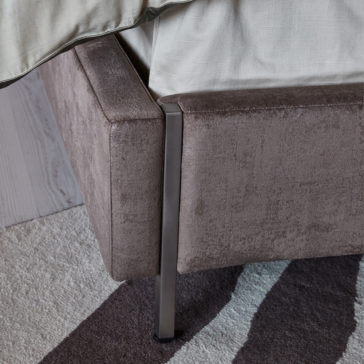 Luxury Metal Frame King Size Bed A close-up view of the Luxury Metal Frame King Size Bed corner, upholstered in soft brown fabric. The sleek metal legs beautifully complement the light beige bedspread. The bed is placed on a rug with a brown and white pattern, enhancing its elegant appeal.