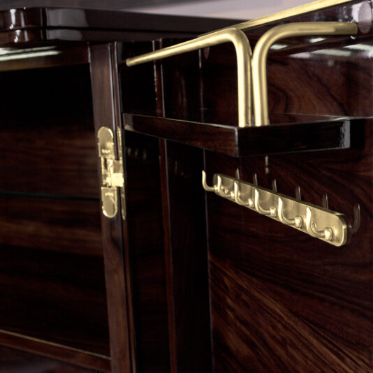 Close-up of the Modern Armoire With Brass Accents featuring open doors that reveal a brass hook rack and polished brass hardware. The hook rack offers multiple hooks for hanging items, and the gleaming brass beautifully contrasts with the rich dark wood finish.