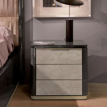Modern Bedside Table With Leather Front A modern bedside table with a dark marble top and three light-colored drawers with a woven texture. A black lamp sits on the table next to a small stack of papers. The background features a framed picture on a gray wall and part of a bed with beige bedding.