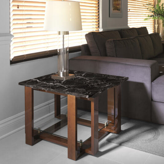 Modern Black Marble Top Side Table A modern living room showcases a Modern Black Marble Top Side Table with a wooden frame, positioned beside a gray sofa. A table lamp with a glass base and white shade is elegantly placed on top of the sleek side table. Blinds partially cover the windows, allowing natural light to illuminate the room.
