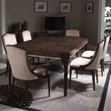 Modern Maple Extendable Dining Table A dining room showcasing the Modern Maple Extendable Dining Table, encircled by six upholstered chairs. Beneath the table lies a patterned rug, while a TV sits on a cabinet against the back wall. The walls are adorned with framed pictures, and potted plants enhance the corners of the room.