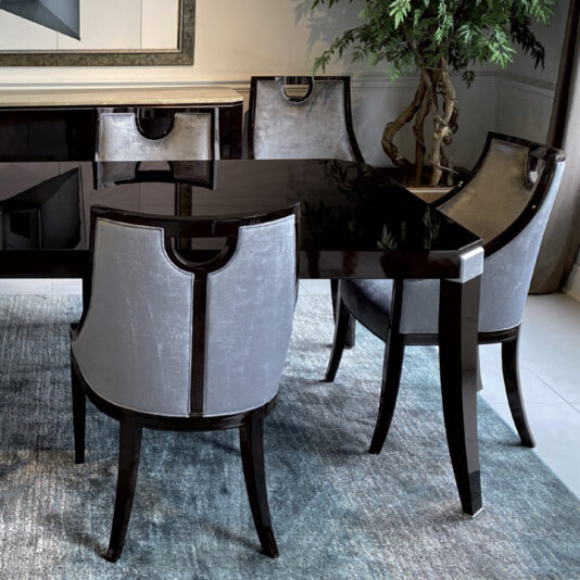 Modern Dark Walnut Dining Table A modern dining set featuring a sleek Modern Dark Walnut Dining Table and four upholstered chairs with dark wooden frames and light gray fabric. The set is placed on a blue rug, accompanied by a stylish modern rosewood sideboard. A potted plant and framed artwork complete the sophisticated scene.