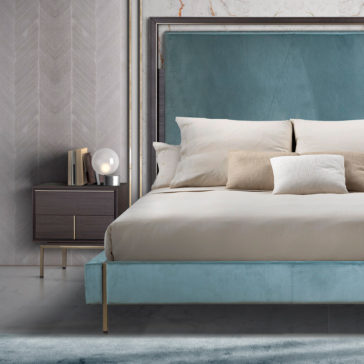 Luxury Leather Horse Handle Bedside Cabinet A modern bedroom featuring a large bed with a teal upholstered headboard and beige bedding. There are three pillows on the bed. Beside the bed is the Luxury Leather Horse Handle Bedside Cabinet, adorned with leather accents and a sleek horse-shaped handle, holding books and a spherical lamp.