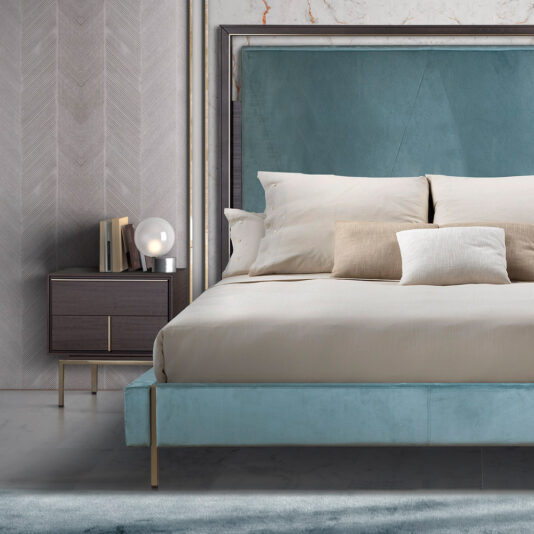 A modern bedroom featuring a large bed with a teal upholstered headboard and beige bedding. There are three pillows on the bed. Beside the bed is the Luxury Leather Horse Handle Bedside Cabinet, adorned with leather accents and a sleek horse-shaped handle, holding books and a spherical lamp.
