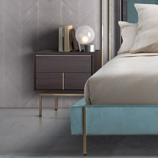 A modern bedroom scene featuring a Modern Elegant Bedside Table with two minimalist wooden drawers, books, and a spherical lamp on top. Next to it is a neatly made bed with beige sheets and pillows. The wall behind has a textured pattern, and the floor is smooth and light-colored.
