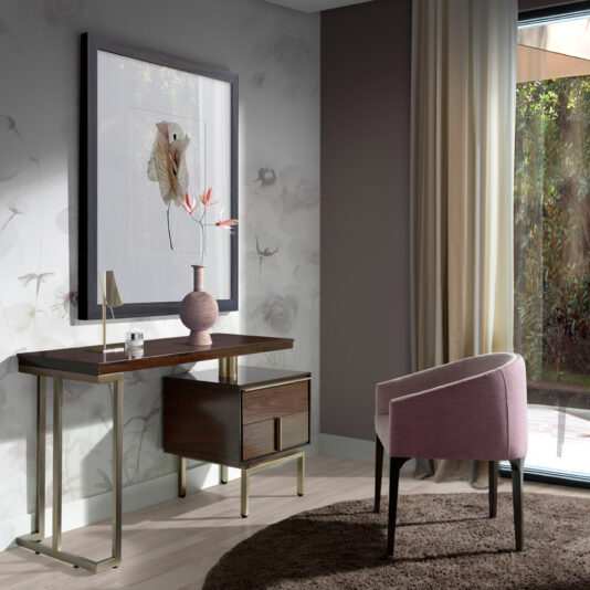 Modern Elegant Dressing Table A modern, minimalist home office featuring the Modern Elegant Dressing Table with a dark wood top, metal legs, and a drawer. The setup is styled with a coordinating pink vase of flowers, a sleek table lamp, and framed artwork. A pink cushioned chair sits on a round brown rug to complete the look.