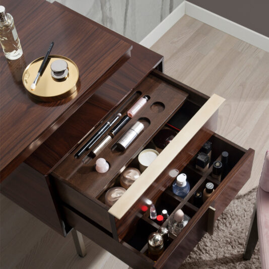 Modern Elegant Dressing Table The Modern Elegant Dressing Table features a sophisticated wooden vanity and an open drawer that neatly organizes makeup and skincare items. A tray on the table holds a perfume bottle, a small black compact, and a brush. The floor is made of light-colored wood, and there's a partially visible pink chair next to it.