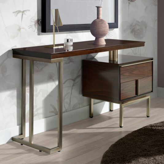 A Modern Elegant Dressing Table with gold metallic legs is placed against a wall with a light floral pattern. On the table are a small lamp, a round decorative vase, and another smaller item. There is also a drawer unit attached beneath the table. A round beige rug lies on the floor below.