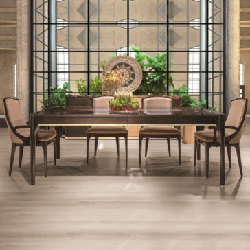 Modern Maple Dining Table Set The Modern Maple Dining Table Set showcases a sleek dark wooden table accompanied by six upholstered chairs. Positioned behind the table, a large industrial-style window provides views of lush green plants. The background is enhanced with a decorative centerpiece and a large circular wall ornament.