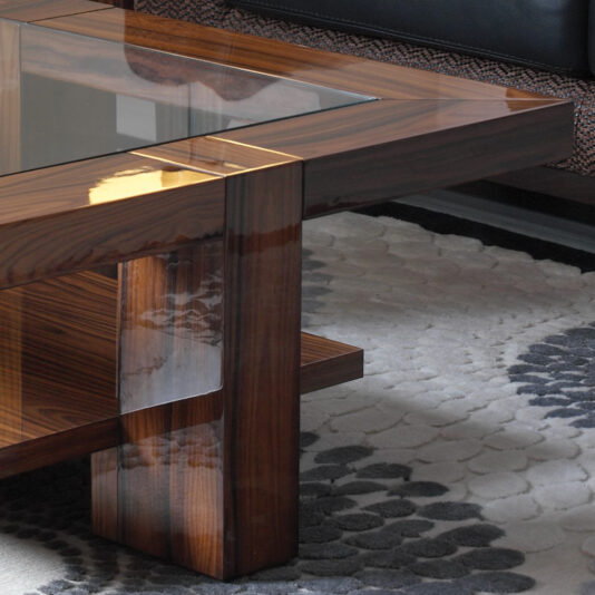 Modern Rectangular Coffee Table With Glass Top A close-up view of the Modern Rectangular Coffee Table With Glass Top showcases its polished dark wood finish and convenient lower shelf. It sits elegantly on a gray and white patterned area rug, with the edge of a black leather couch visible in the background.