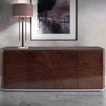 The Modern Rosewood Sideboard, featuring a sleek design and a striking radial wood grain pattern, stands against a light-grey wall. On the left end of the sideboard sits a table lamp with a cylindrical beige shade. Above it, a framed black-and-white cityscape photograph is mounted on the wall.