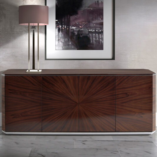 The Modern Rosewood Sideboard, featuring a sleek design and a striking radial wood grain pattern, stands against a light-grey wall. On the left end of the sideboard sits a table lamp with a cylindrical beige shade. Above it, a framed black-and-white cityscape photograph is mounted on the wall.