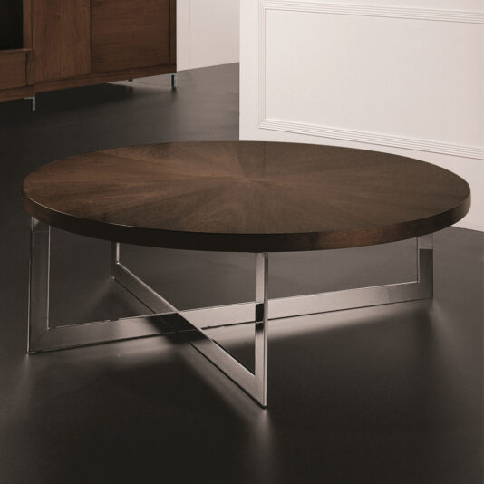 A Modern Round Coffee Table showcasing a polished dark wood top and a sleek metal base with intersecting legs, set against a dark floor with a white-paneled wall in the background.