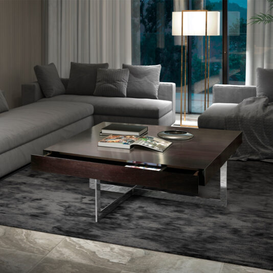 A modern living room with a gray L-shaped sofa, a large Modern Square Coffee Table With Drawers, and a tall floor lamp. The coffee table holds magazines, books, a metallic tray, and other decorative items. The room features large windows with floor-to-ceiling curtains.