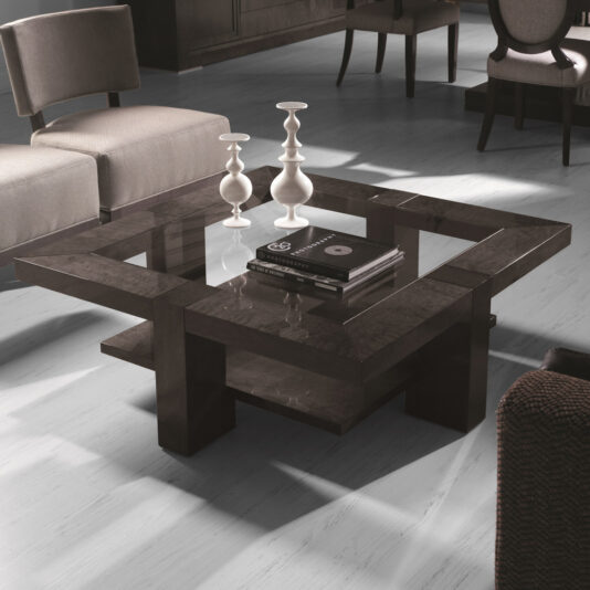 A modern living room showcases the sleek Modern Square Coffee Table With Glass Top, tastefully adorned with white candlesticks, a book, and a small bowl. The table sits on a light-colored floor and is surrounded by contemporary chairs and a woven texture seat in a dimly lit ambiance.