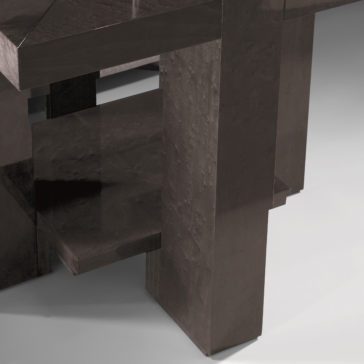 Modern Square Side Table With Glass Top A close-up of the corner of the Modern Square Side Table With Glass Top, showcasing its sleek, dark-colored design. The table features geometric, angular legs and a shiny glass top, all set against a plain, light background.