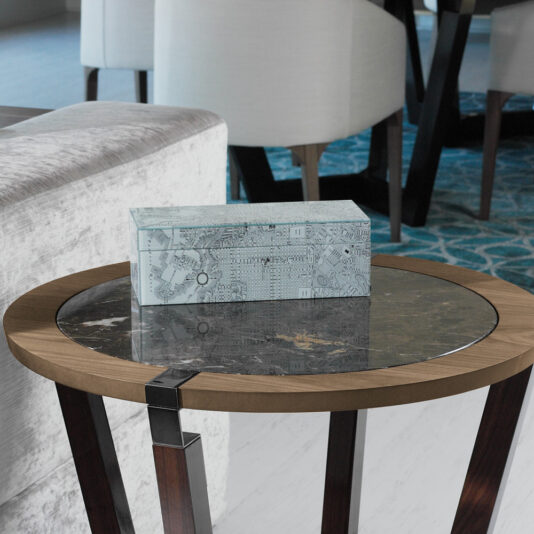 A rectangular patterned glass box is placed on a Modern Stylish Side Table with a glass top. The round wooden table stands next to a light gray sofa, and a patterned blue rug is partially visible in the background along with contemporary dining chairs.