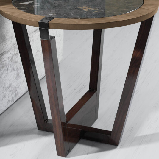 Introducing the Modern Stylish Side Table, featuring a round wooden top with a glass insert at its center. This table boasts a unique geometric dark wood base adorned with metal accents. Perfect for various interiors, it stands beautifully on light-colored flooring next to a textured light gray wall.