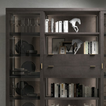 Modern Stylish Wooden Bookcase The Modern Stylish Wooden Bookcase with glass doors is filled with various items. The shelves display neatly arranged wine glasses, plates, books, framed pictures, and decorative horse statues. Warm lighting accentuates the elegance of the contents.