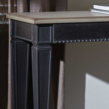 A close-up of the corner of the Modern Two-Tone Wooden Console Table showcases its dark wooden legs and lighter tabletop. The table features detailed trim and edge design. Partially visible on top is a stack of books, with a curtain and a portion of a wall in the background.
