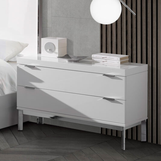 A sleek, modern **Modern Miami Style Large White Bedside Table** with two drawers and minimalist metallic handles is positioned against a textured gray wall with wooden slats. A contemporary white lamp hangs above it, while a geometric decor piece accompanied by a small dish sits on the tabletop. Part of a bed is visible on the left.
