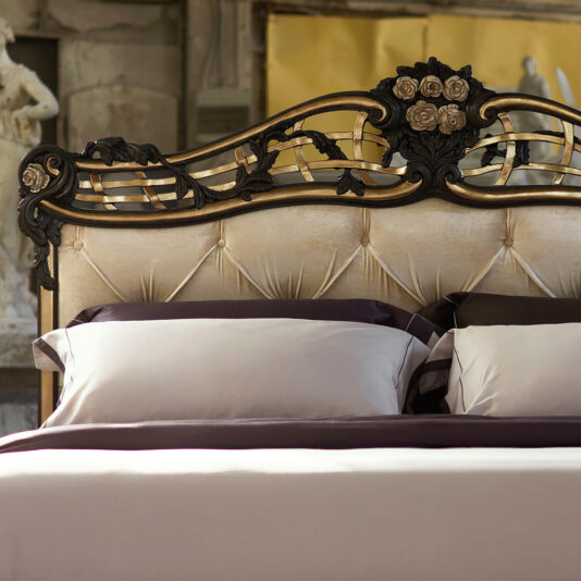 Ornate Button Upholstered Italian Bed The Ornate Button Upholstered Italian Bed boasts a luxurious and intricately carved dark wooden headboard adorned with exquisite floral details. The stunning headboard contrasts beautifully with the light-colored, button-tufted upholstery. The bed is impeccably made with coordinating light-colored pillows and a matching bedspread, perfectly complementing the elegance of the room.
