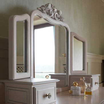 Ornate Italian Dressing Table The Ornate Italian Dressing Table is a stunning wooden vanity featuring an elaborate mirror with three sections. The central rectangular mirror is flanked by two smaller side mirrors, creating a beautifully coordinated look. This exquisite piece includes drawers with round knobs and has bottles of perfume and decorative items elegantly placed on top.