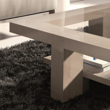 A modern **Maple Veneer Rectangular Coffee Table With Glass Top** and wooden frame sits on a black shaggy rug. A light-colored couch is partially visible in the background, and a white book with a blue cover is stored on the lower shelf of the table.