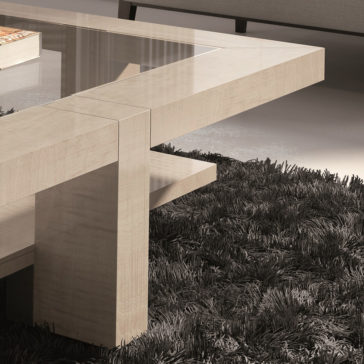 A close-up of the Maple Veneer Rectangular Coffee Table with Glass Top showcases its modern design featuring unique corners. The table is set on a textured dark gray rug and holds part of a book. In the background, there is a sofa and a glossy floor.