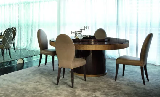 A modern dining room boasts a round dark wood table and four upholstered chairs resting on a light gray rug. Sheer floor-to-ceiling curtains and a large wall mirror enhance the elegant ambiance of the space.