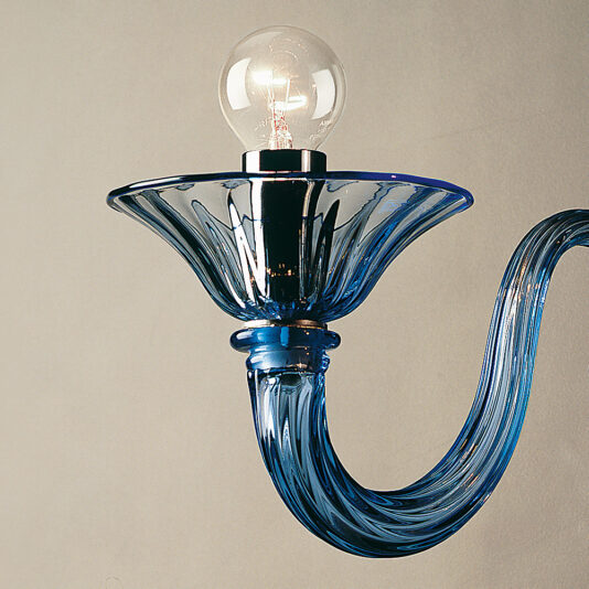 Classic Blue Glass Ribbed Detail Wall Light The Classic Blue Glass Ribbed Detail Wall Light features a stylish wall-mounted design with a curving arm and a flared bowl-shaped shade, holding a clear light bulb. The intricate ribbed detail in the glasswork adds elegance and modernity to the piece.