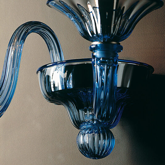 Classic Blue Glass Ribbed Detail Wall Light A close-up of the Classic Blue Glass Ribbed Detail Wall Light, showcasing its intricately designed swirling arm and bowl-shaped holder. Both elements exhibit exquisite ribbed details and reflective surfaces, all mounted against a plain background.