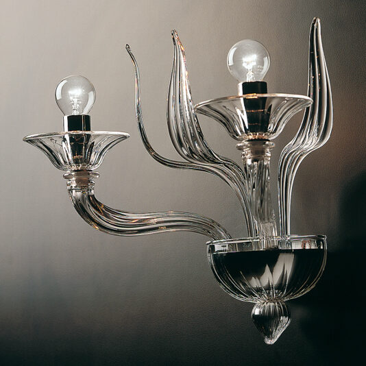 The Classic Clear Glass Ribbed Detail Wall Light is a sophisticated wall sconce featuring two exposed light bulbs encased in intricately designed, clear glass fixtures. Its ribbed detail design boasts elegant, flowing curves that resemble stylized, elongated leaves or petals, all set against a dark background.