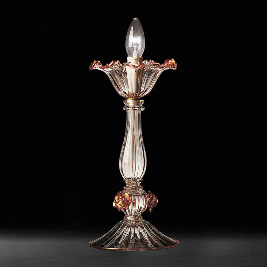 The Classic Floral Detail Table Lamp boasts an elongated, transparent glass body adorned with gold accents and a charming floral-inspired design. Its lampshade mimics a blooming flower with intricate petal details, showcasing a visible light bulb at the top. Set against a black background, its exquisite floral detail is beautifully highlighted.