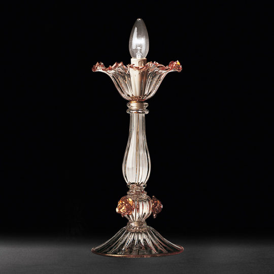 The Classic Floral Detail Table Lamp boasts an elongated, transparent glass body adorned with gold accents and a charming floral-inspired design. Its lampshade mimics a blooming flower with intricate petal details, showcasing a visible light bulb at the top. Set against a black background, its exquisite floral detail is beautifully highlighted.