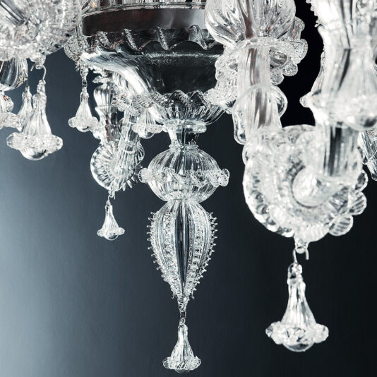Close-up of the Classic Glass Chandelier With Floral Detailing. The chandelier showcases delicate, ornate glass patterns and hanging glass drops, creating a luxurious and elegant appearance. The dark background highlights the clarity and craftsmanship of the glass.