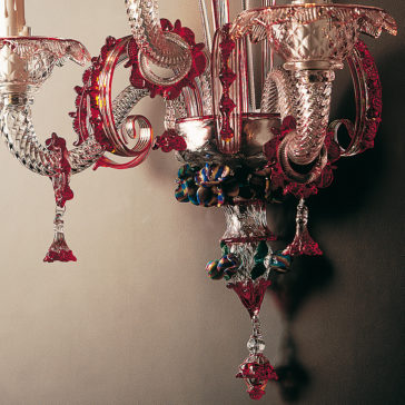Classic Glass Wall Light With Red Floral Detailing A stunning Classic Glass Wall Light With Red Floral Detailing hangs against a wall. This ornate, vintage chandelier showcases intricate designs with clear and red floral accents, complete with candle-like extensions. The light is both elaborate and decorative, casting warm illumination and shadow patterns on the wall behind it.